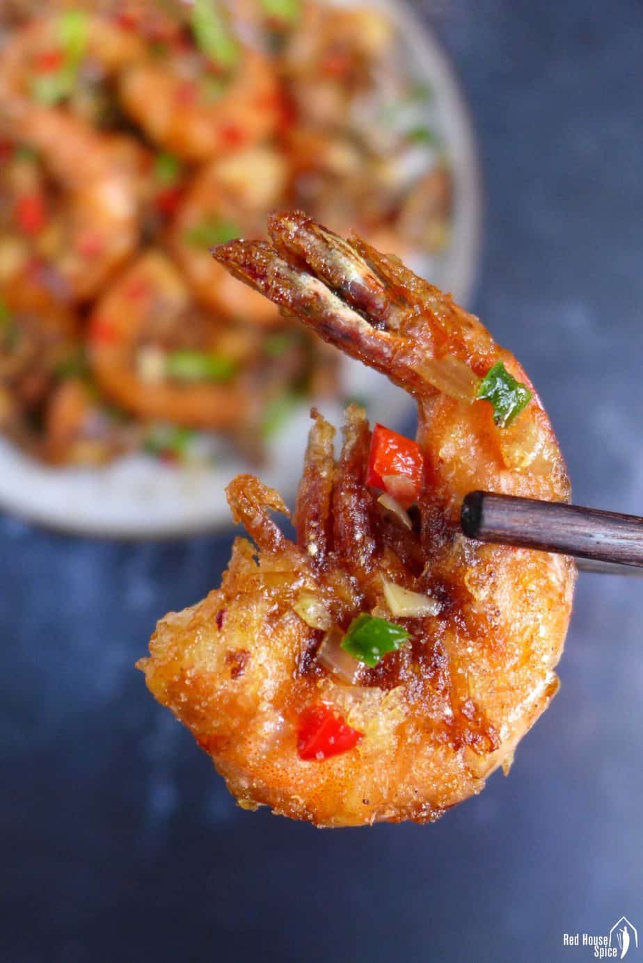 A piece of salt and pepper shrimp held by chopsticks