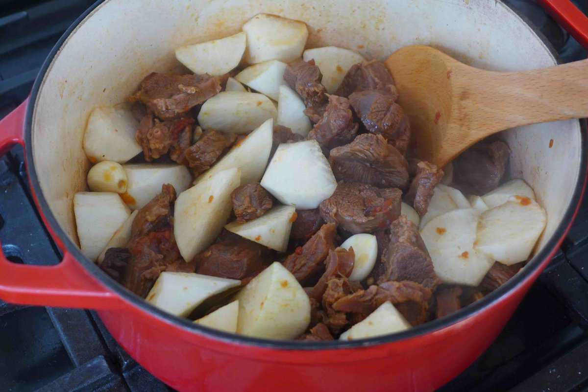 adding daikon to beef in a pot.