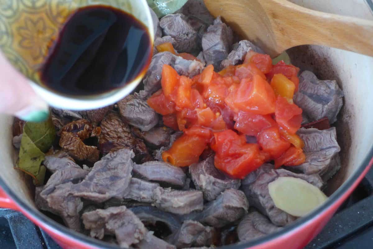 adding chopped tomato and sauce to beef.