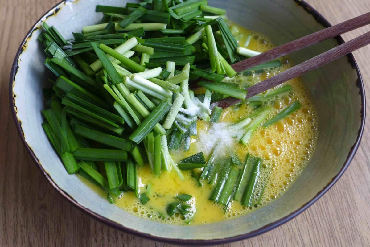 adding chopped chives and salt to beaten eggs.