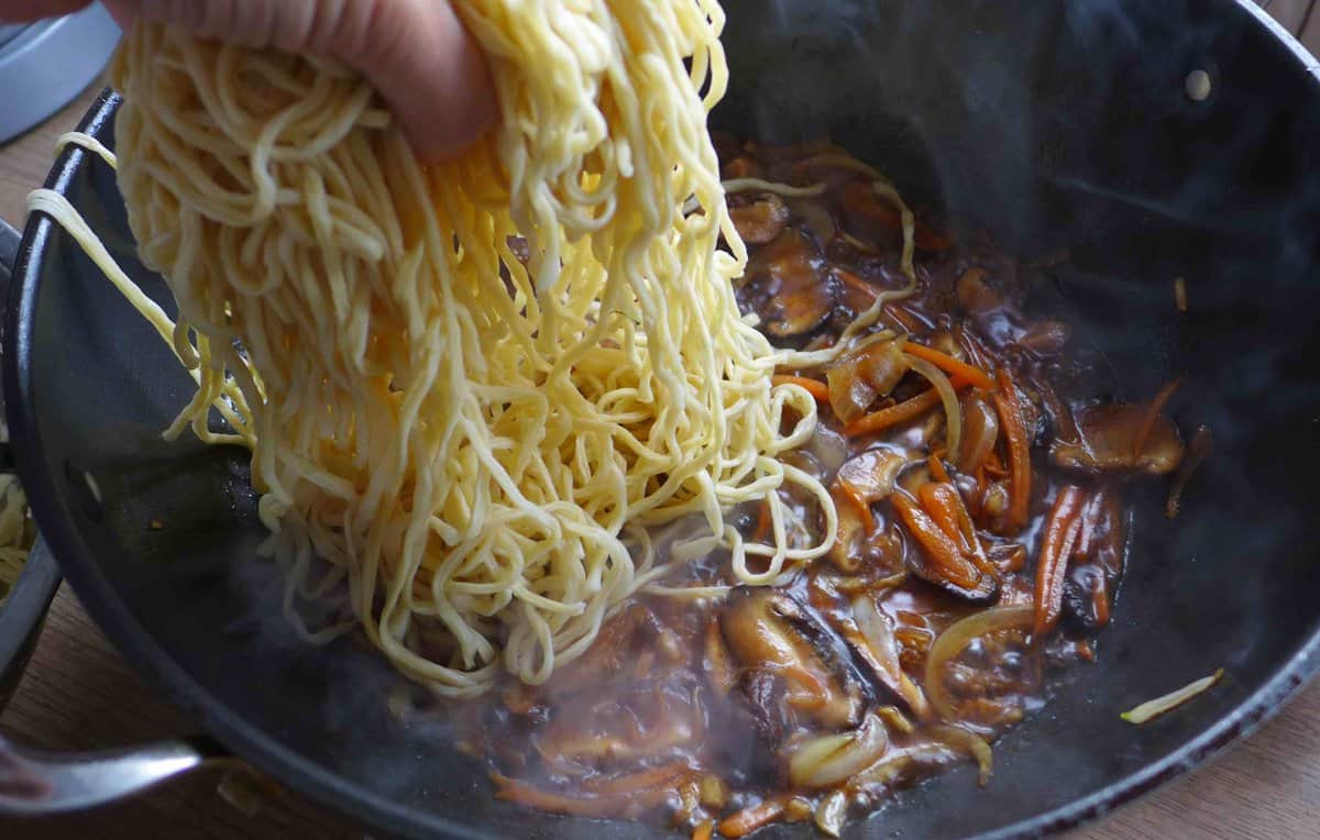 adding cooked noodles to vegetables and sauce.