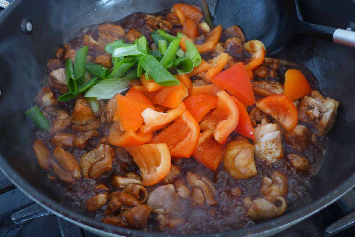 adding bell pepper and scallions to chicken.