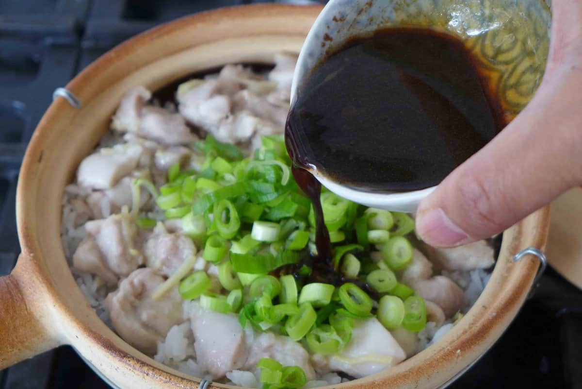 pouring sauce over chicken clay pot rice.