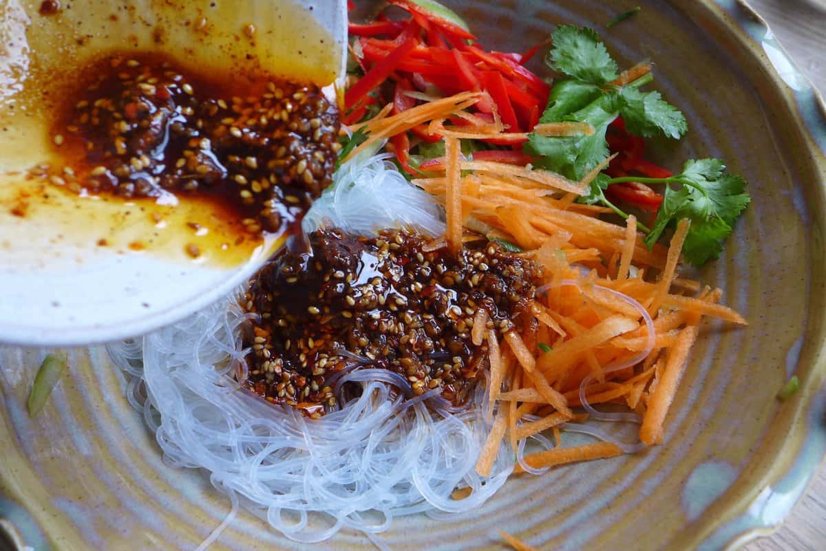 Pouring sauce over noodles and vegetables.