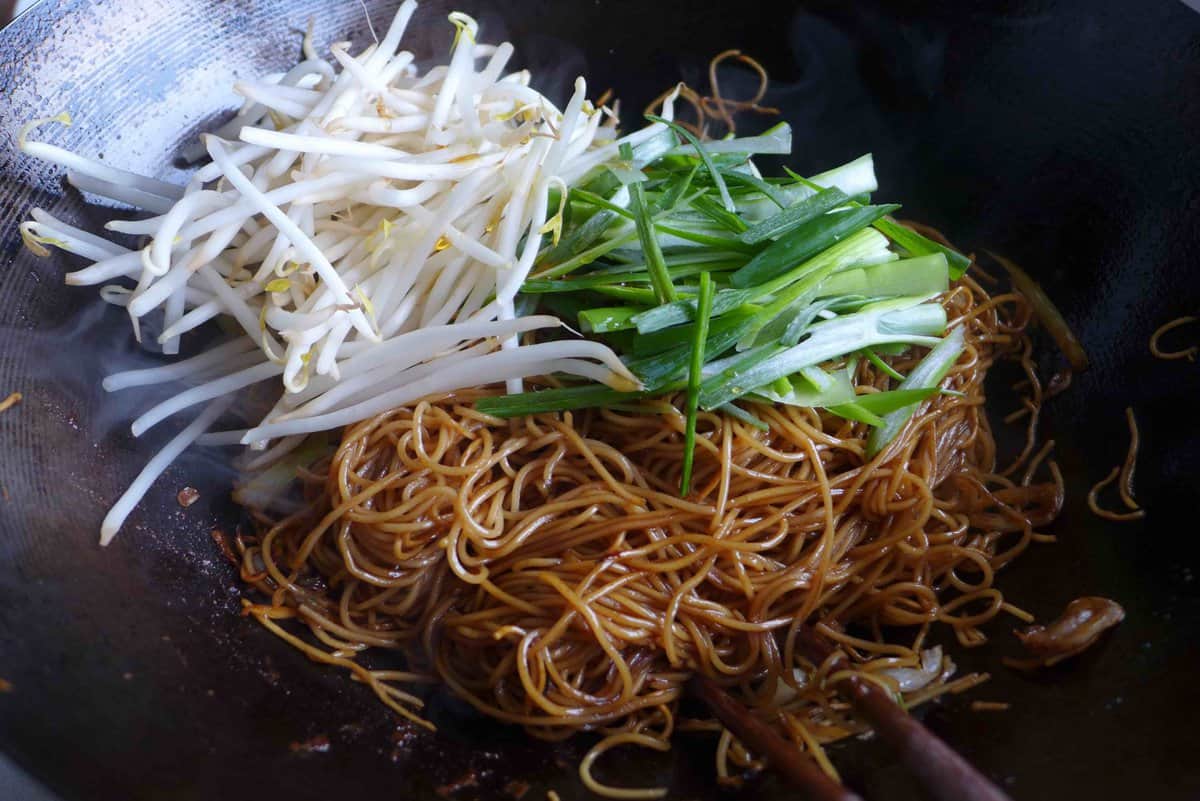 adding bean sprouts and scallions to noodles.