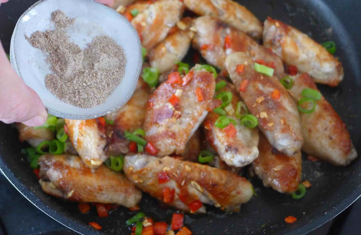adding salt and pepper seasoning to pan-fried chicken wings.
