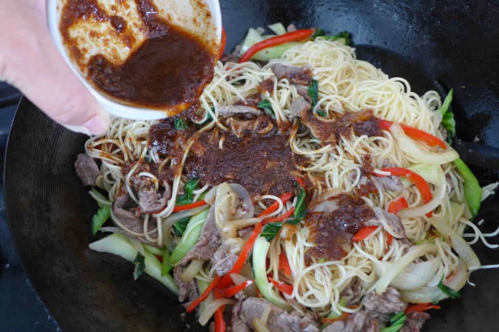 adding sauce to fried noodles with beef.