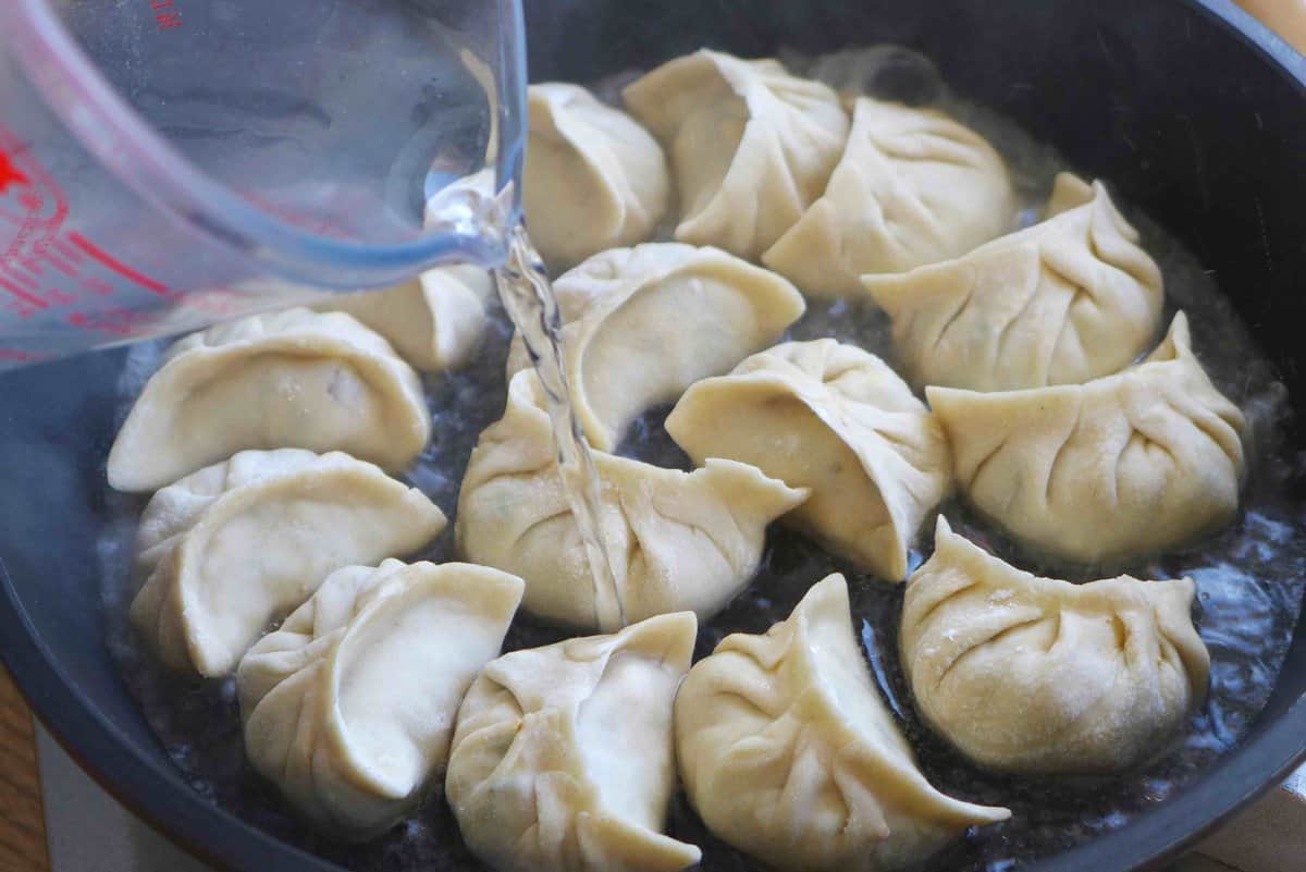 adding water to a skillet with dumplings.