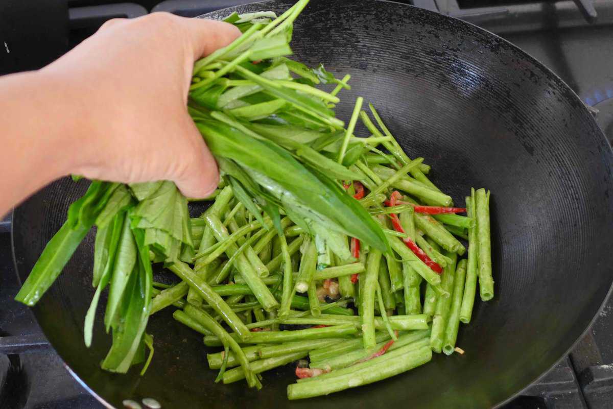 adding water spinach leaves to a wok