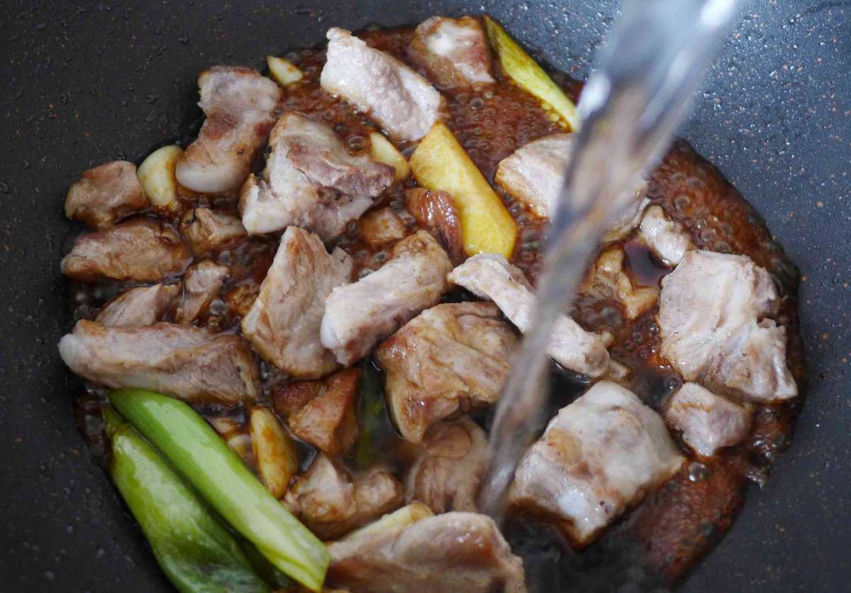 pouring hot water into a wok with ribs and aromatics