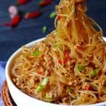 A pair of chopsticks pick up some vermicelli noodles.