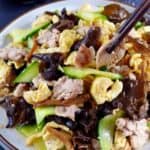 Chopsticks picking up a piece of pork from a plate of Moo Shu Pork