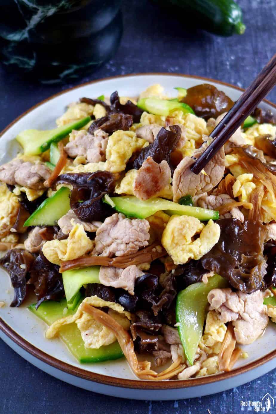 Chopsticks picking up a piece of pork from a plate of Moo Shu Pork