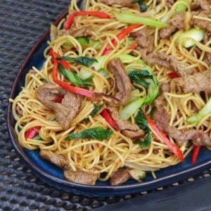 a plate of beef chow mein with sha cha sauce.