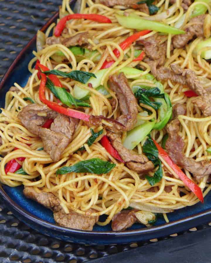a plate of beef chow mein with sha cha sauce.