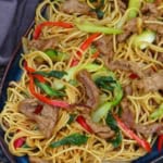 a plate of beef chow mein with sha cha sauce.