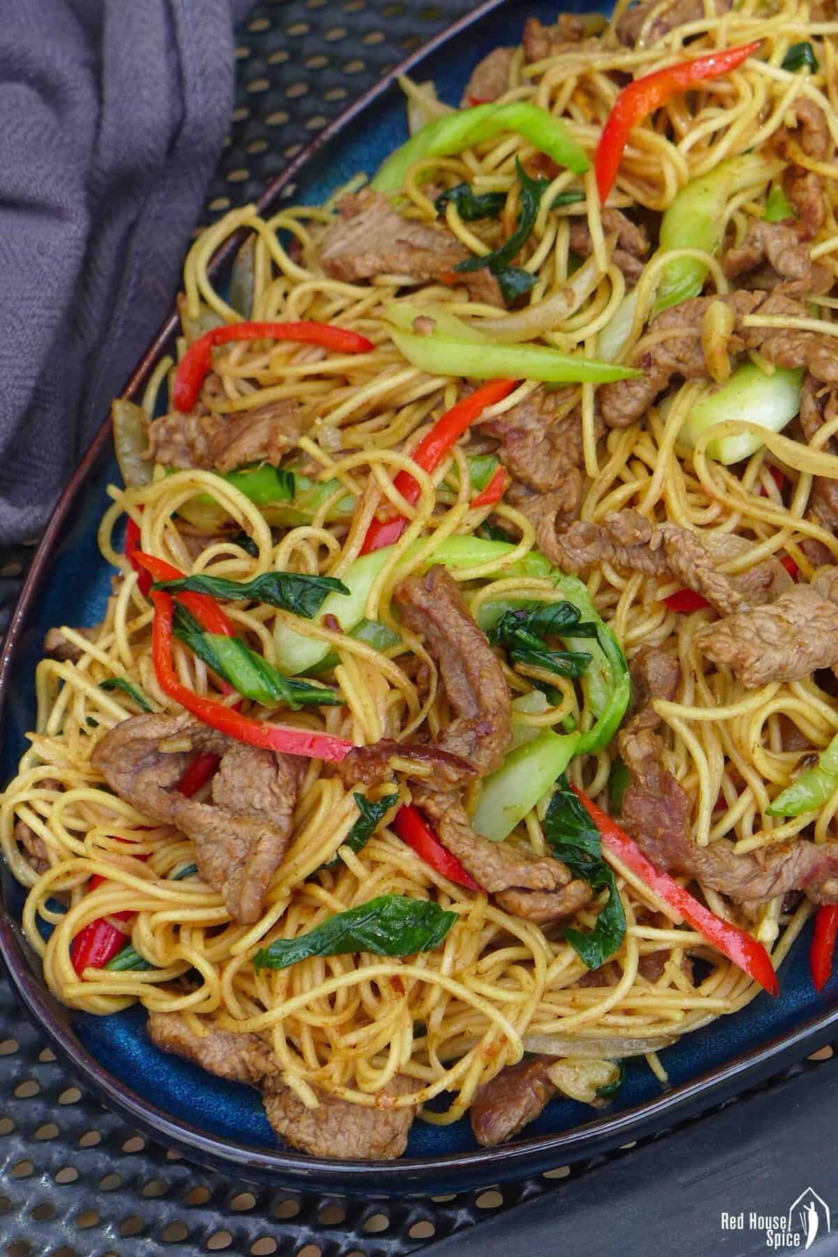 a plate of beef chow mein with sha cha sauce.