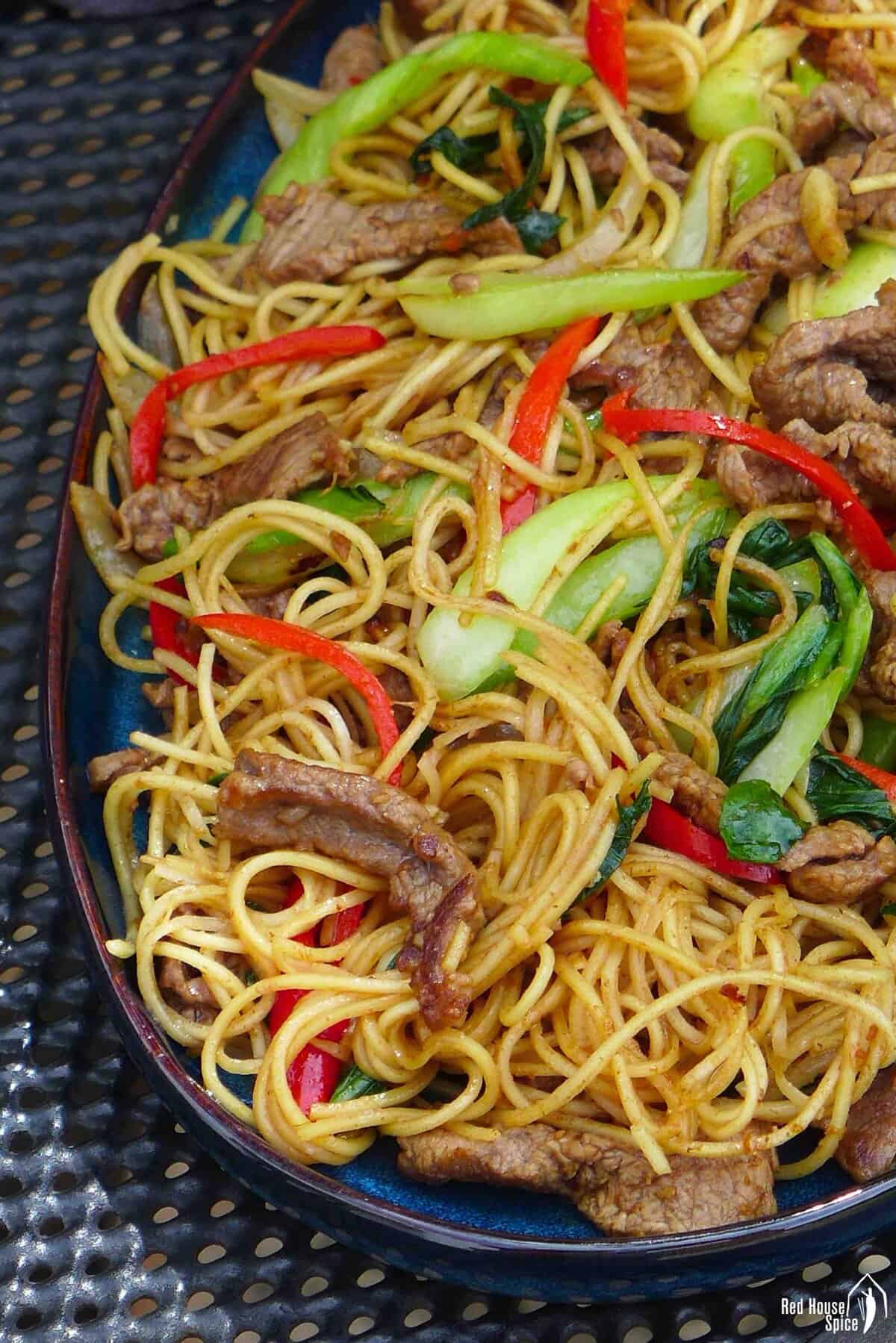a plate of beef chow mein with sha cha sauce.