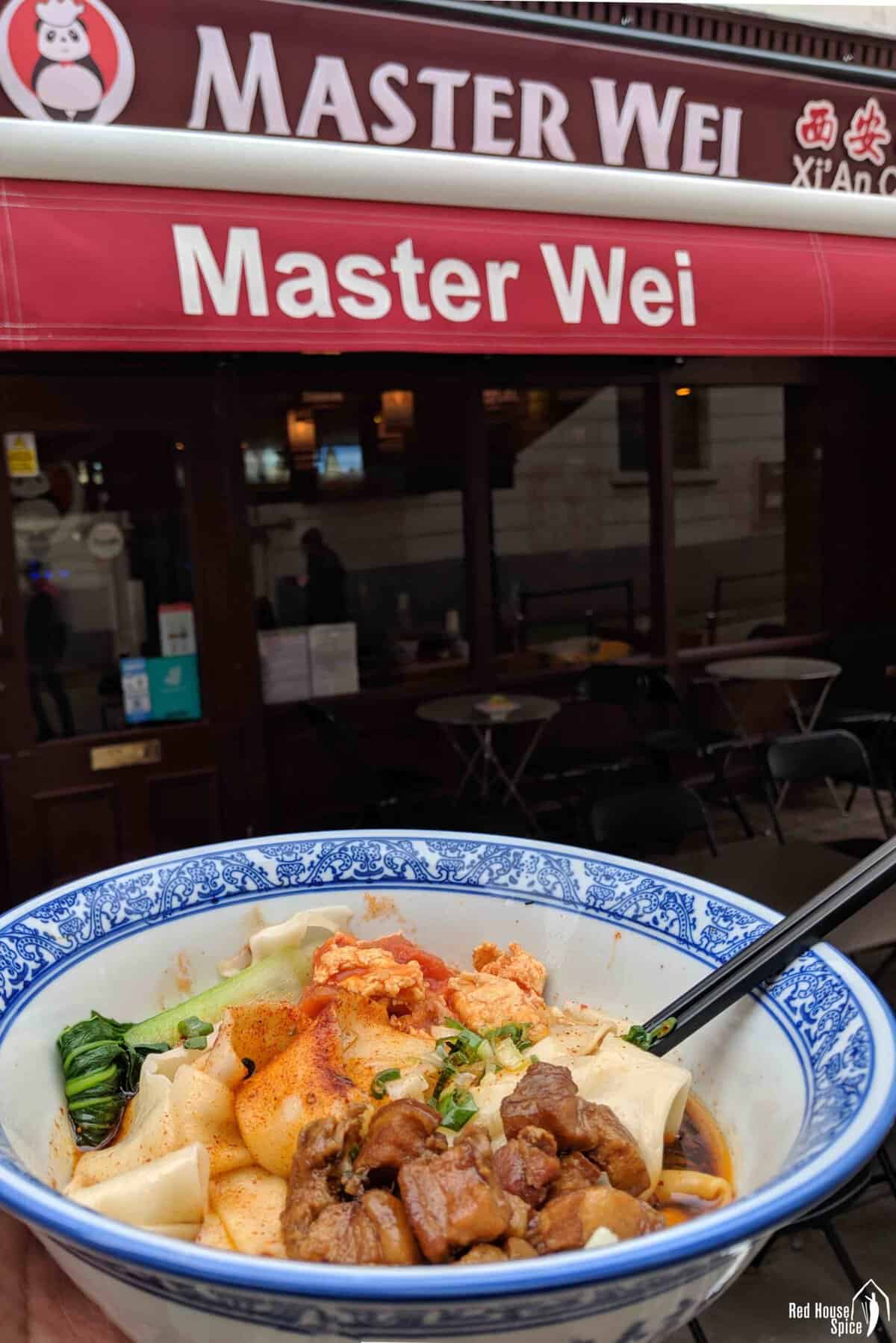 a bowl of Biang Biang noodles in front of restaurant Master Wei.