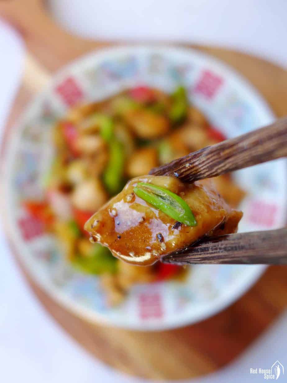 A piece of black pepper chicken held by chopsticks