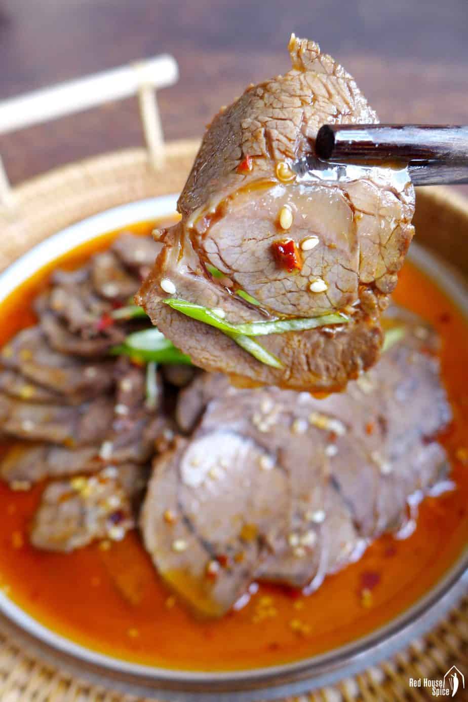 a slice of braised beef shank picked up by a pair of chopsticks