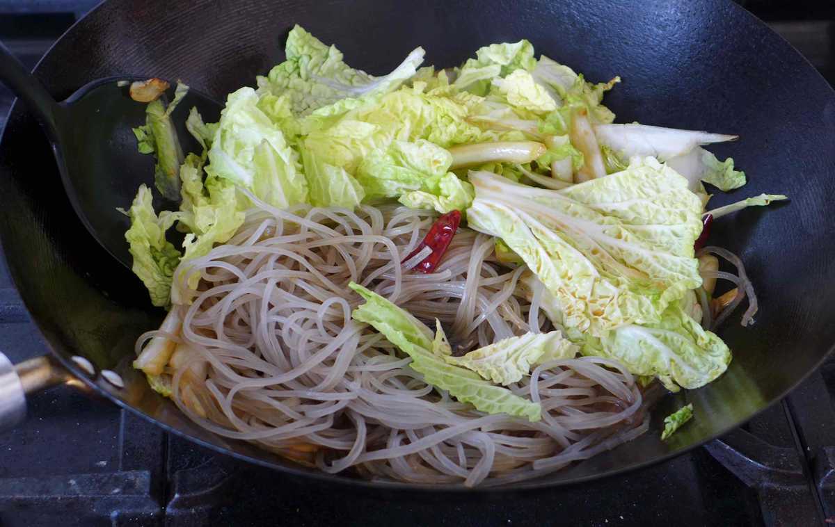 putting Napa cabbage leaves and rehydrated glass noodles in a wok