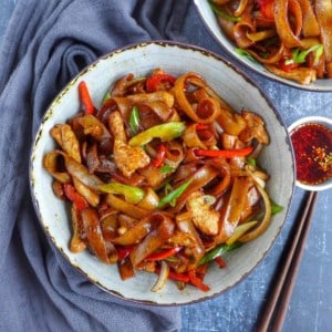 a bowl of chicken chow fun with chili oil on the side.