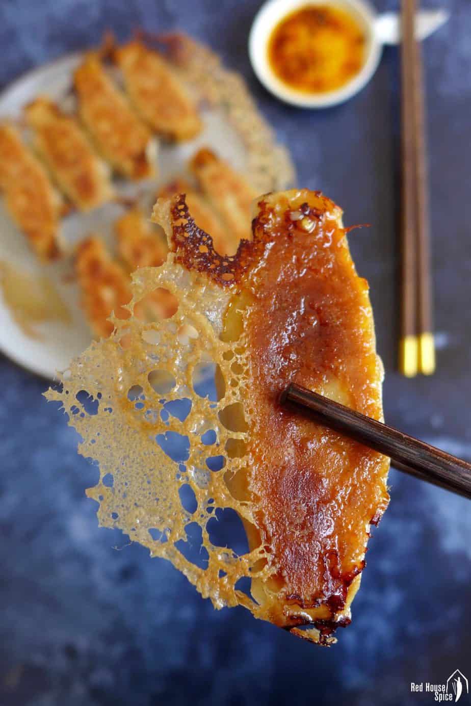 A pan fried dumpling held by a pair of chopsticks