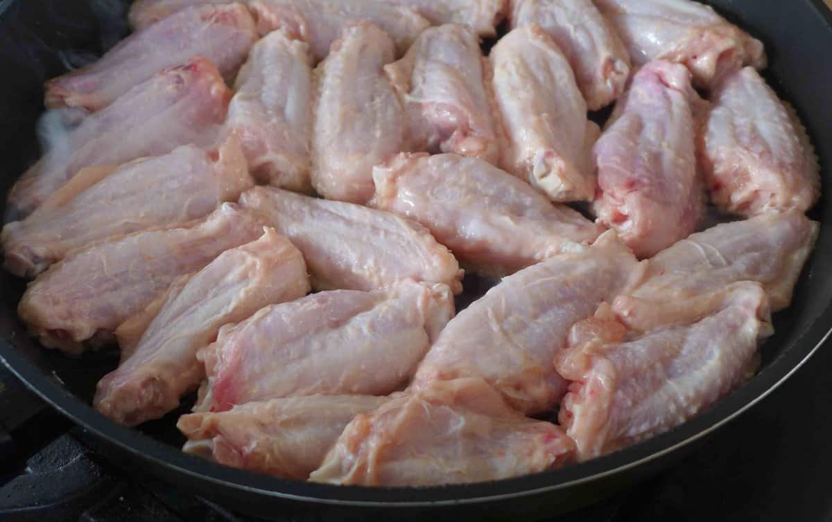 raw chicken wings in a skillet.