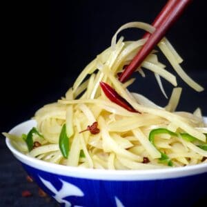 A pair of chopsticks picking up some stir-fried potatoes.