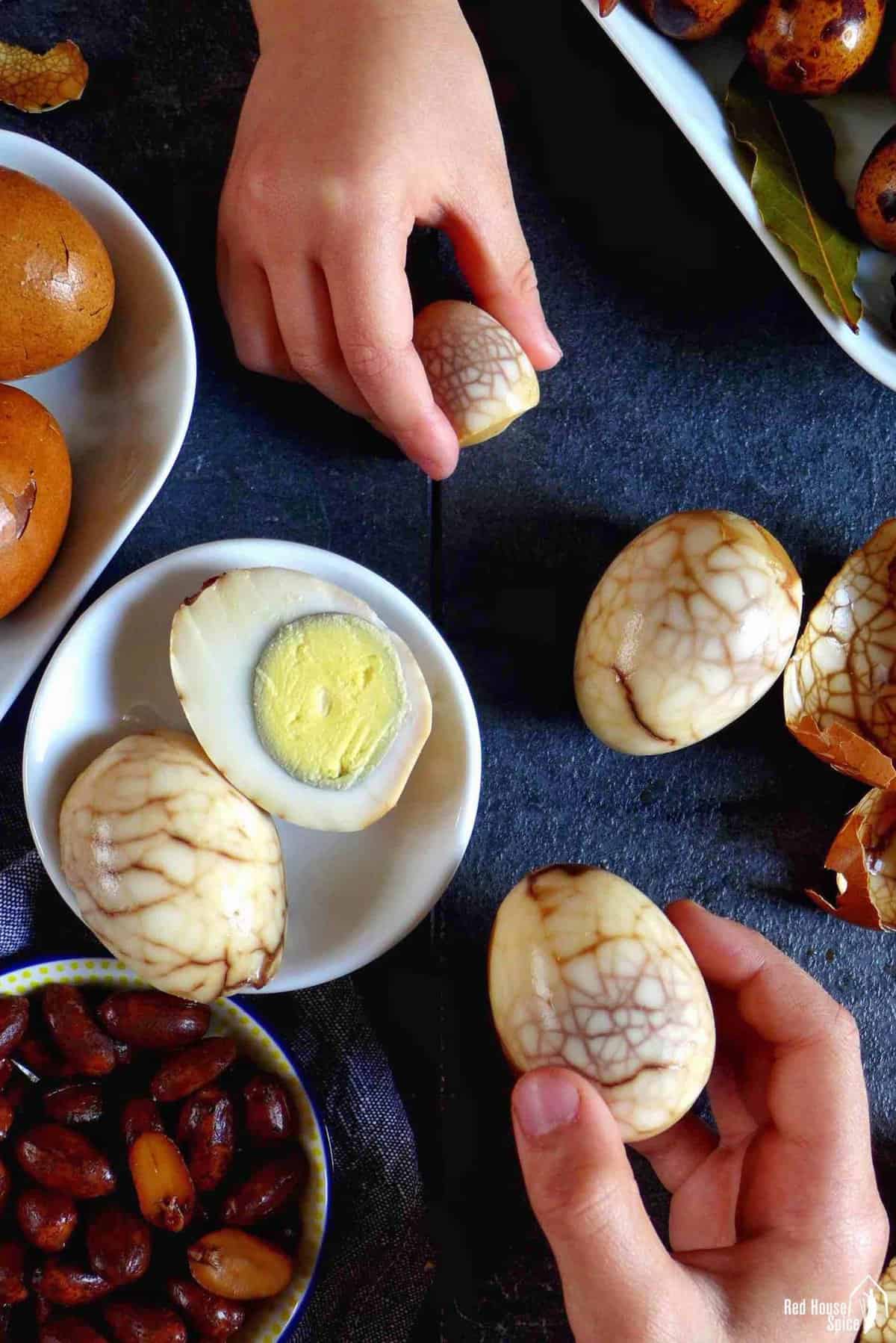 two hands holding a tea marinated hen egg and a tea marinated quail egg.