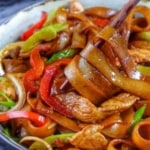 chopsticks picking up wide rice noodles cooked with chicken and vegetables with overlay text that says chicken chow fun.