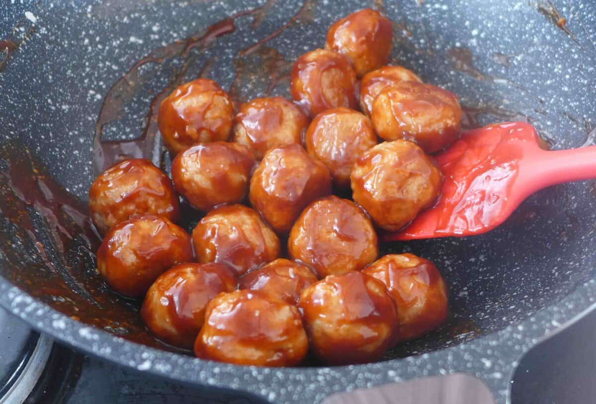 coating meatballs with sweet and sour sauce.