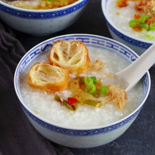 a bowl of plain congee with toppings like fried dough, preserved mustard stem and pork floss
