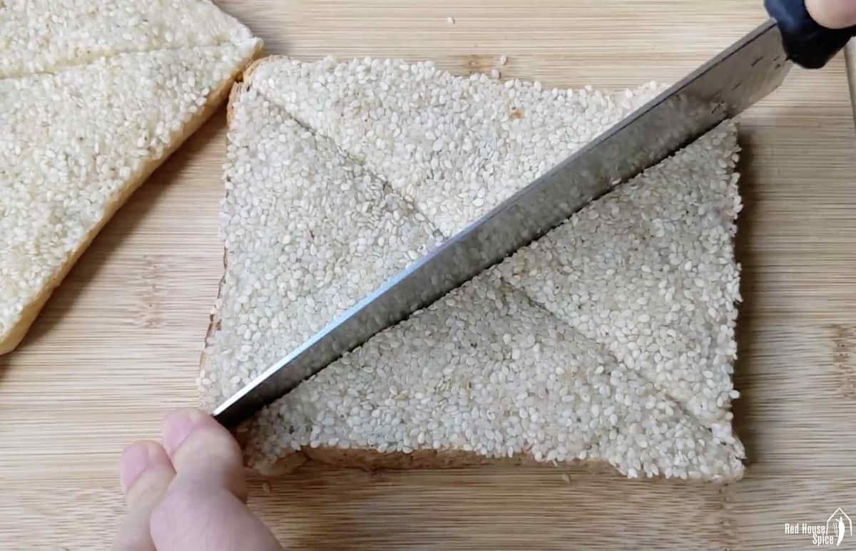 Cutting a piece of uncooked shrimp toast into triangle shaped pieces