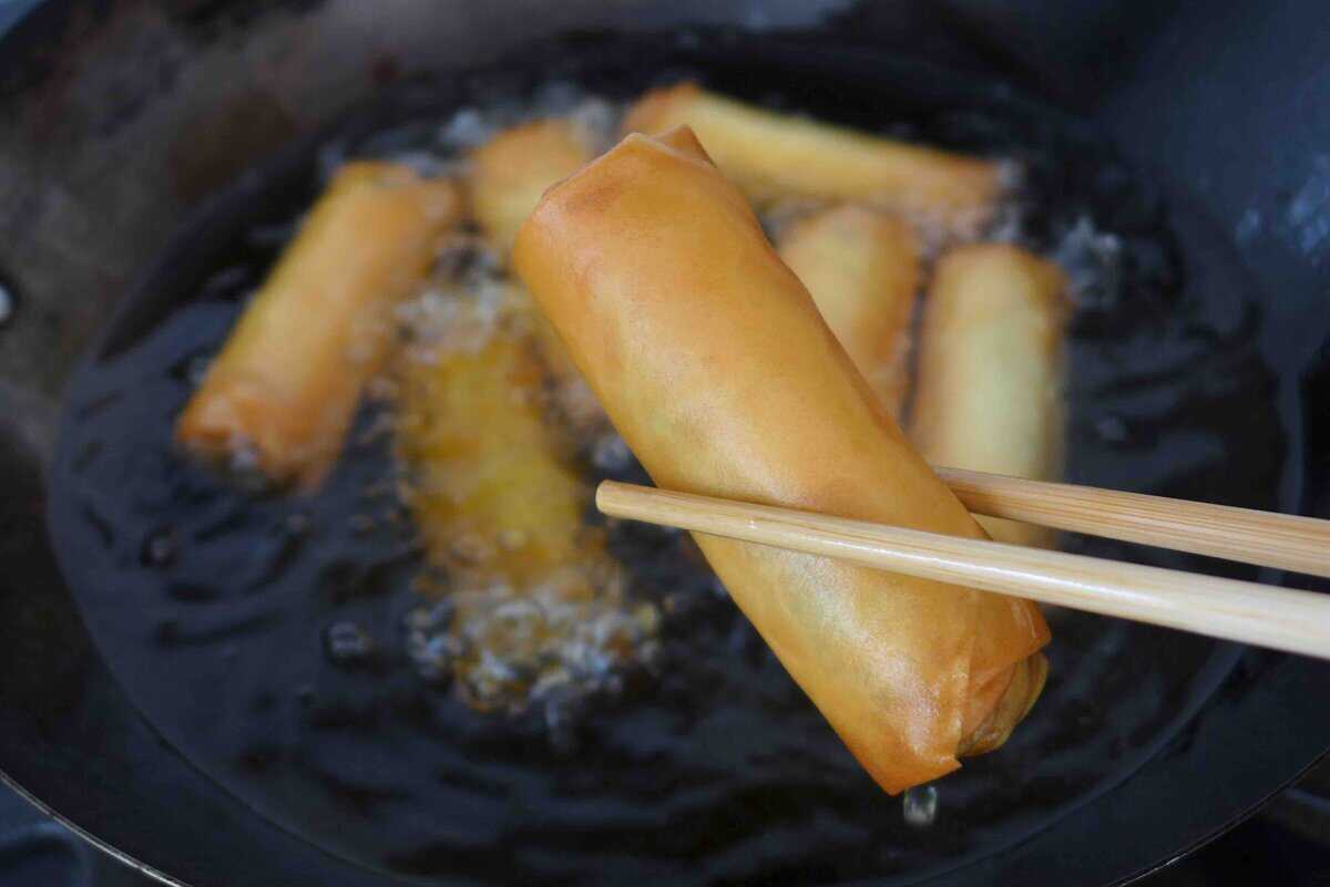 chopsticks holding a deep fried spring roll.