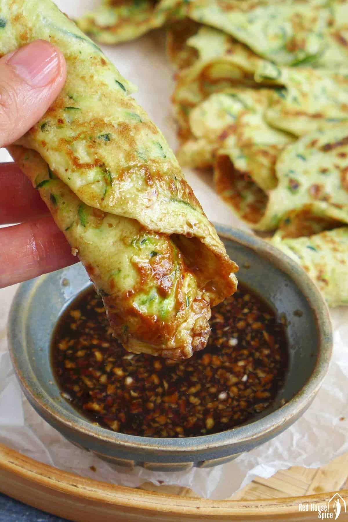 dipping a zucchini pancake into sauce.