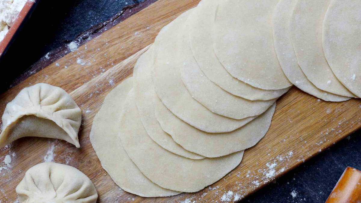 freshly rolled dumpling wrappers with two uncooked dumplings on the side.
