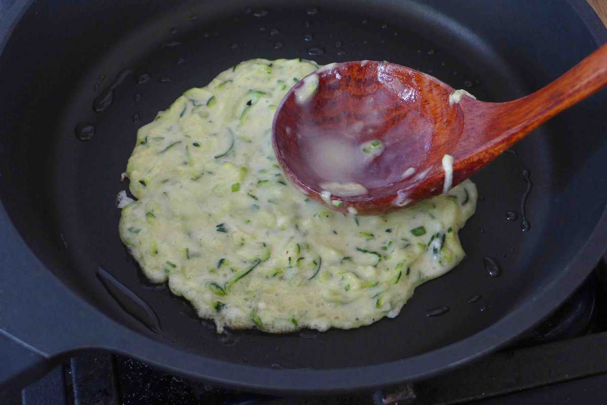 flattening zucchini pancake batter with a spoon.