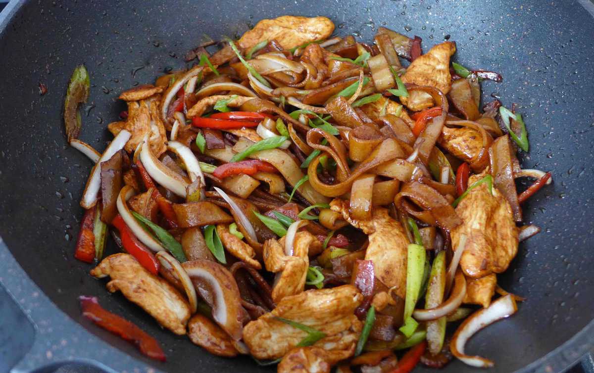 frying chicken, vegetable and rice noodles in a wok.