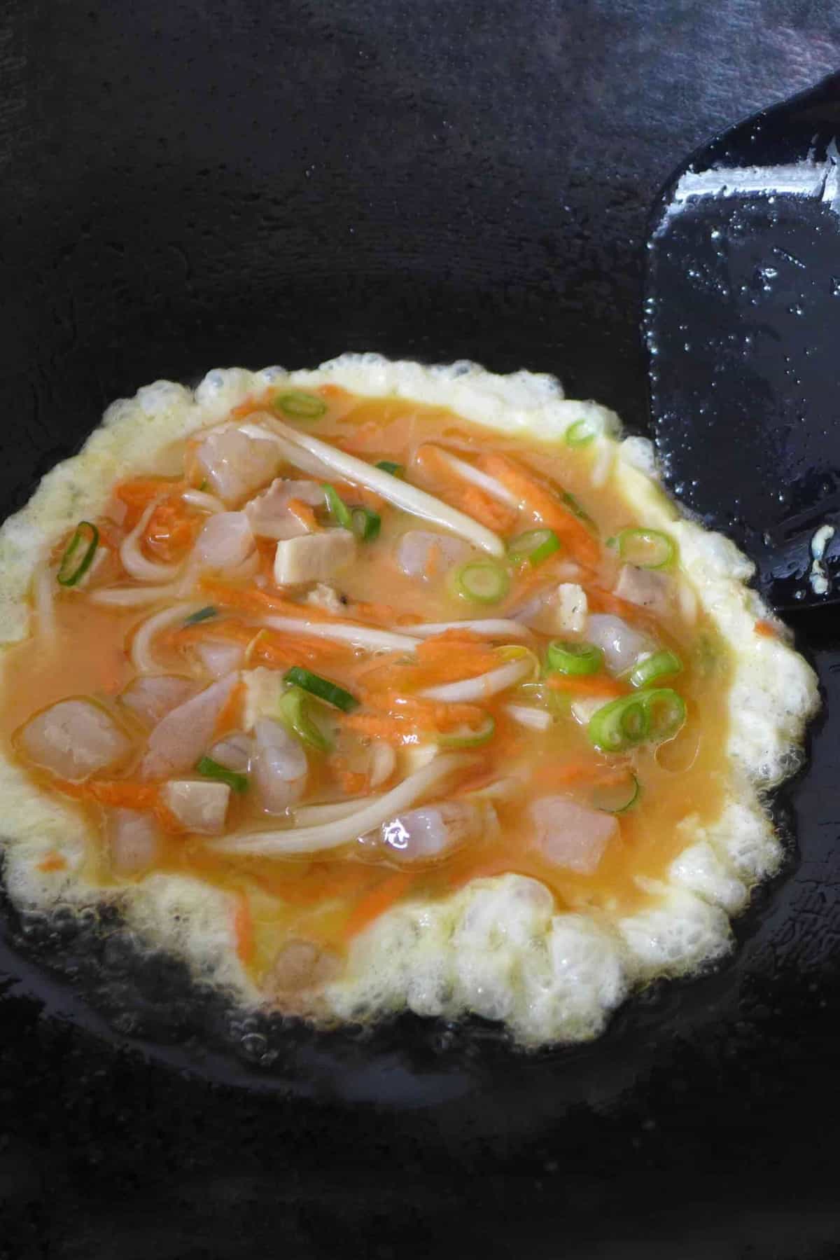 frying a mixture of eggs, shrimp, chicken and vegetables