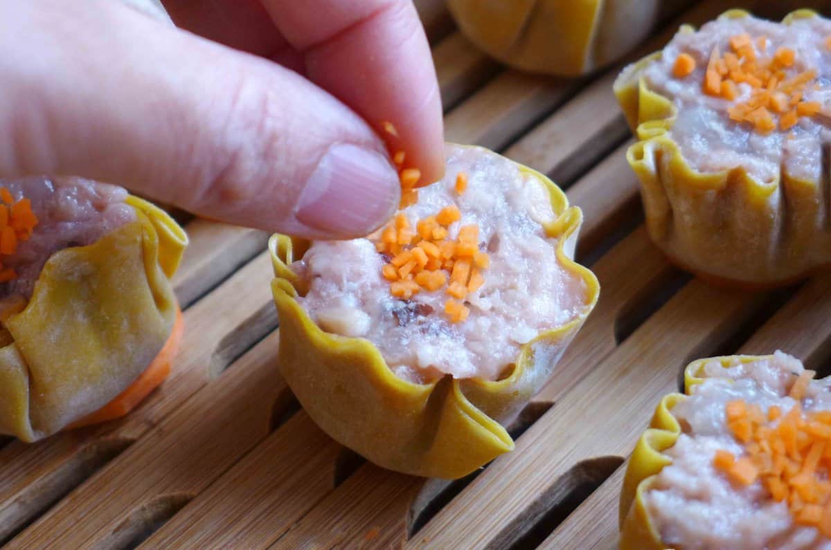 Garnishing Siu Mai with minced carrots.