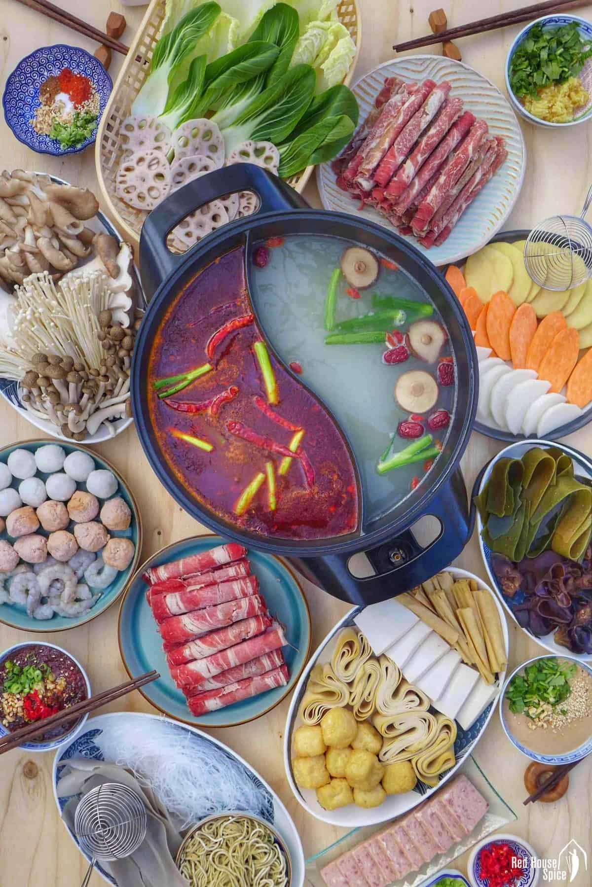 A divided hot pot surrounded with various raw ingredients