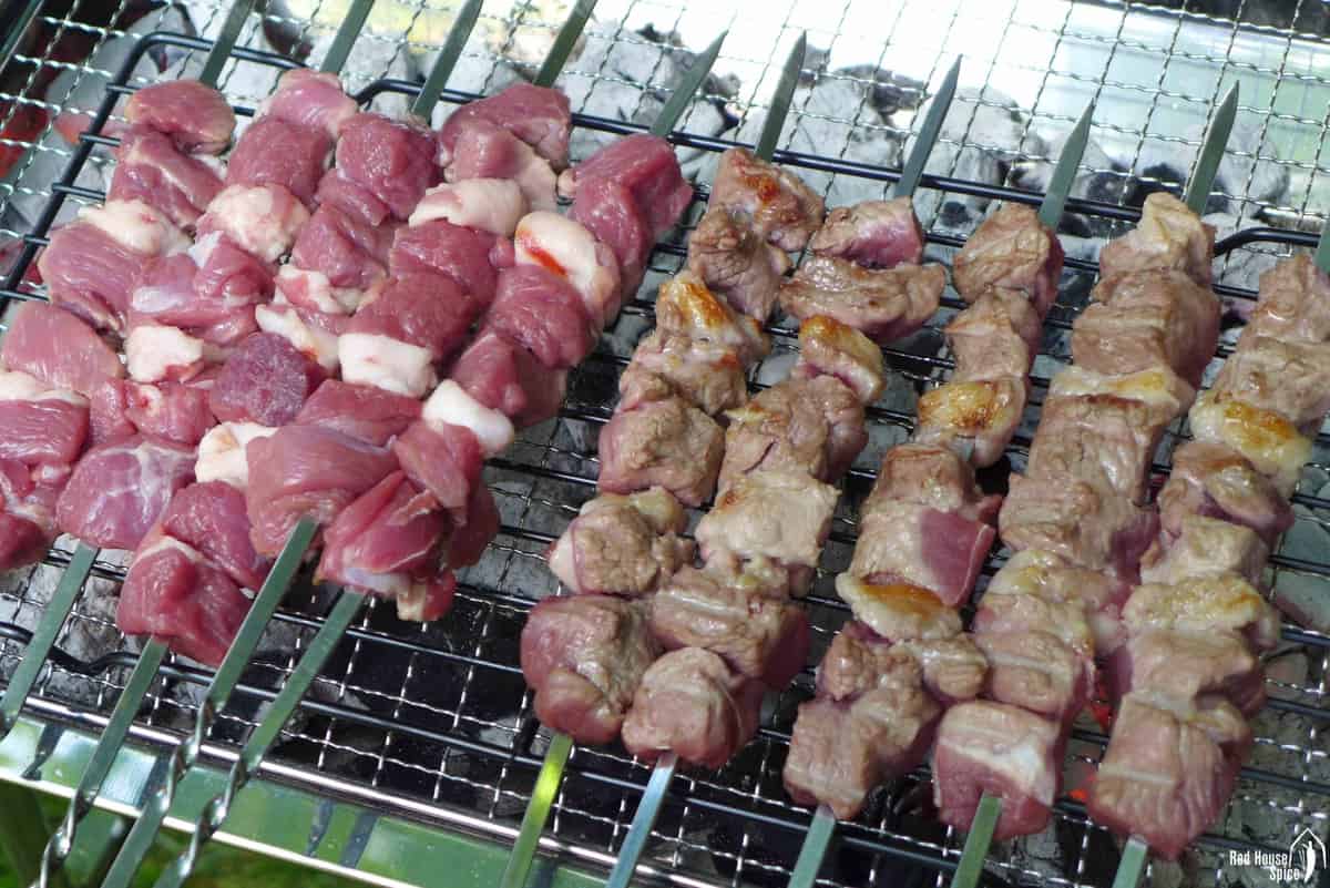 Grilling raw lamb on skewers over charcoal