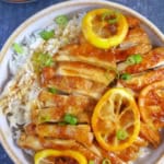 Sliced chicken and lemon over a bowl of rice with overlay text that says lemon chicken.