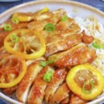 Sliced chicken and lemon over a bowl of rice.