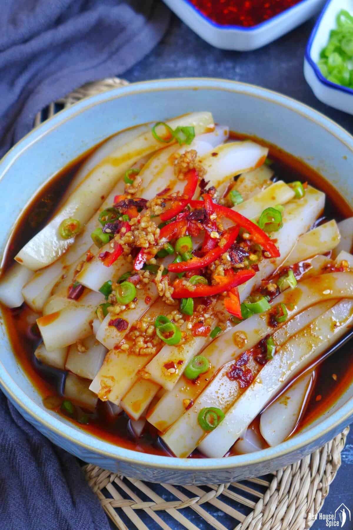 Mung bean jelly noodles in a dark sauce with scallions and chili on top.