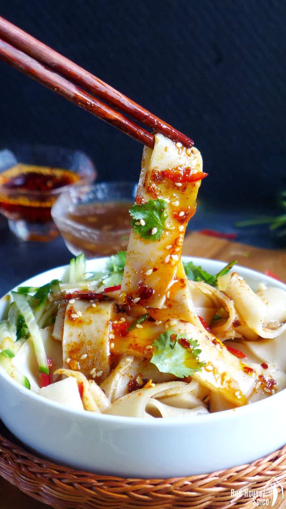 A strip of Liang Pi (cold skin noodles) picked up by a pair of chopsticks. It's covered by chilli oil.