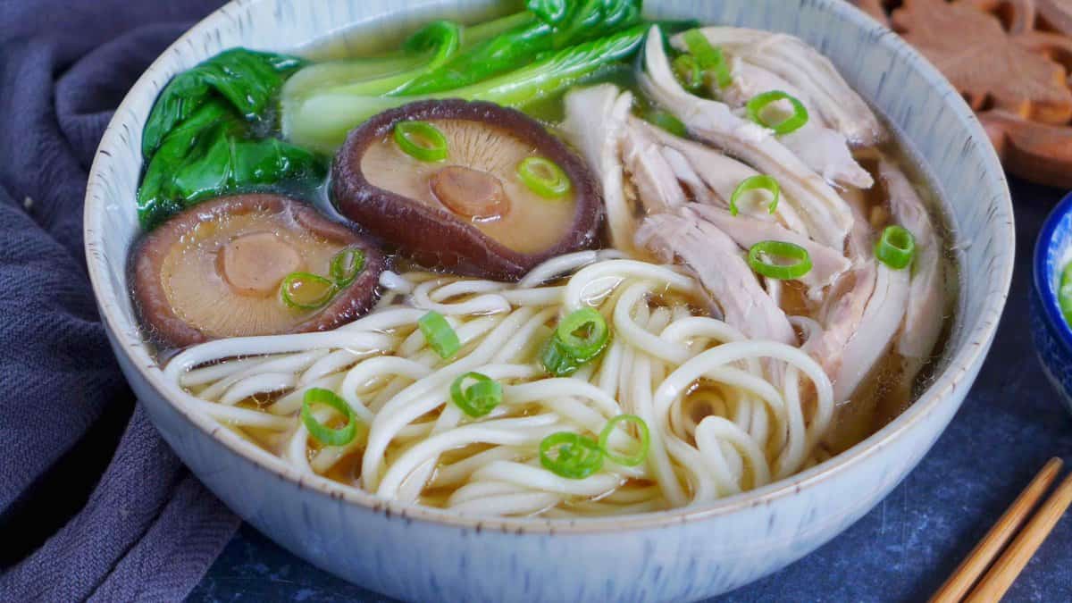 a bowl of chicken noodle soup with shiitake mushrooms and Bok Choy.