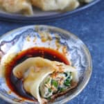 a half-eaten pork and chive dumpling in dipping sauce.